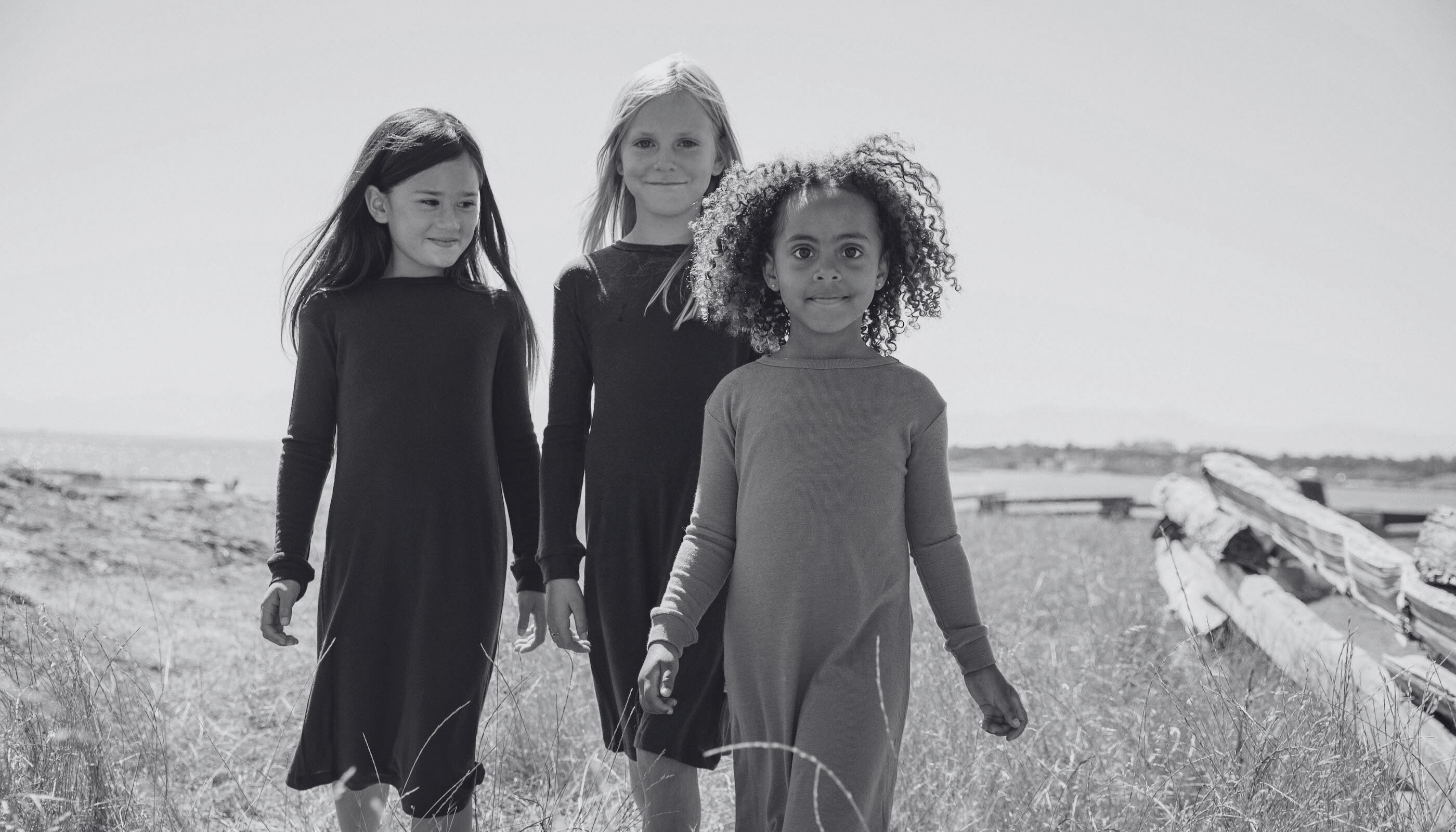 Three children  standing in a field with a wooden fence in the background.
