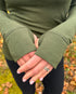 Person wearing a green long-sleeve top with thumbholes standing outdoors in the fall.