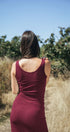 Woman in a red tank and skirt standing in an outdoor setting with trees and clear sky